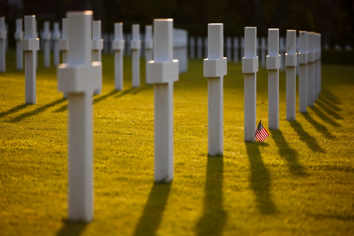 Rows of white marble cross headstones on green grass with American flag