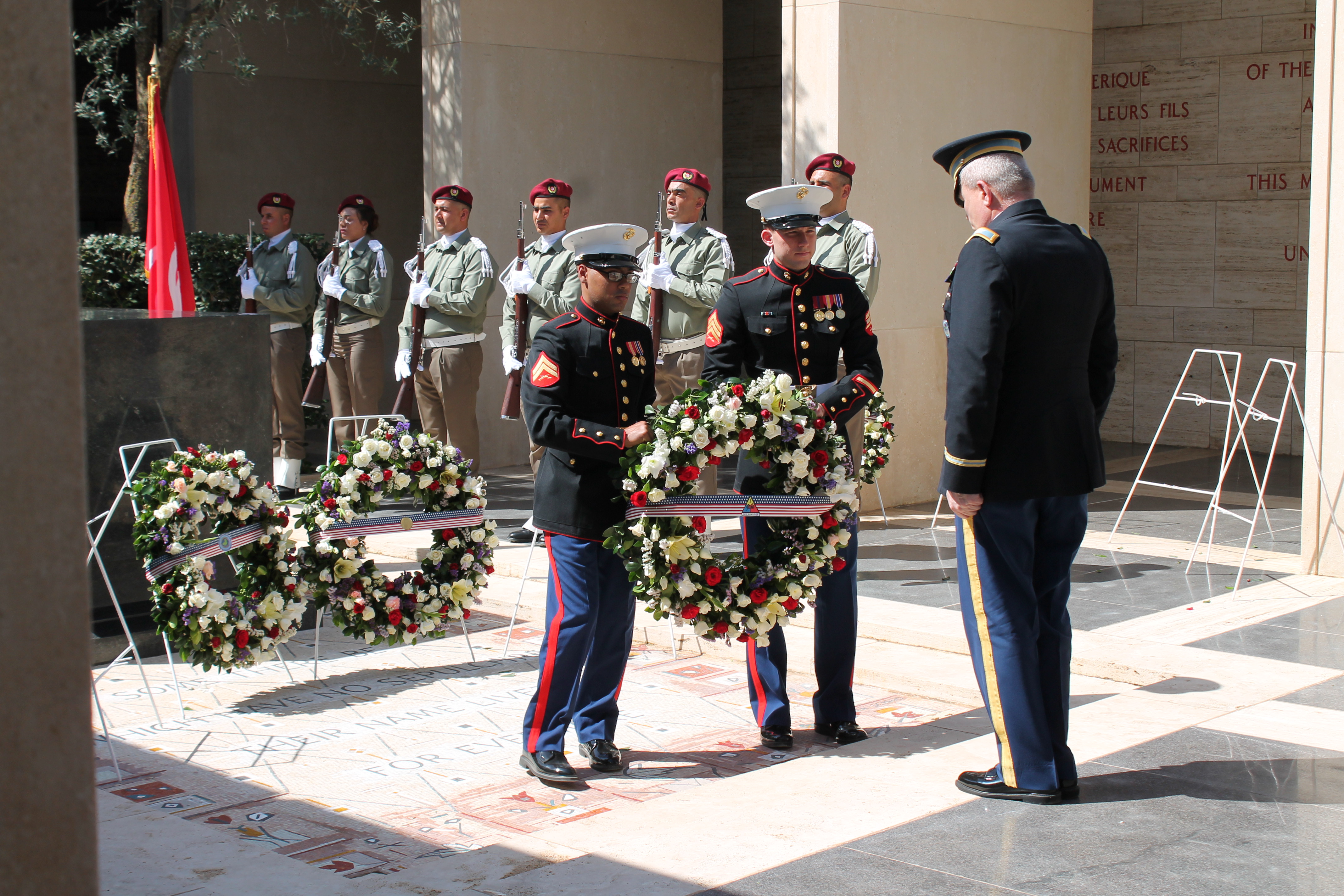 Two Marines present a floral wreath to a man in uniform. 