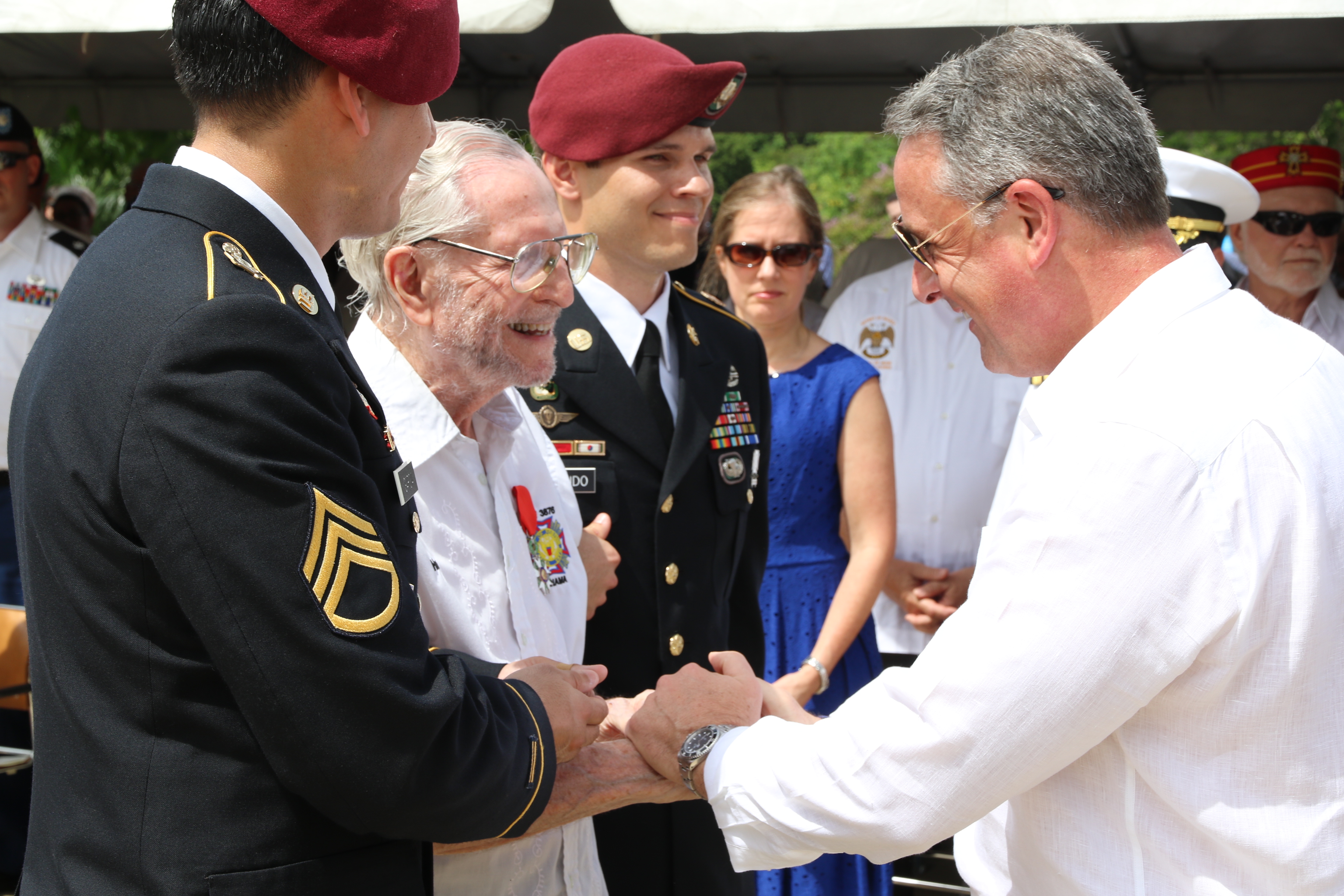 The U.S. Ambassador shakes hands with Herbert Friedlander, who is flanked by two American soldiers. 