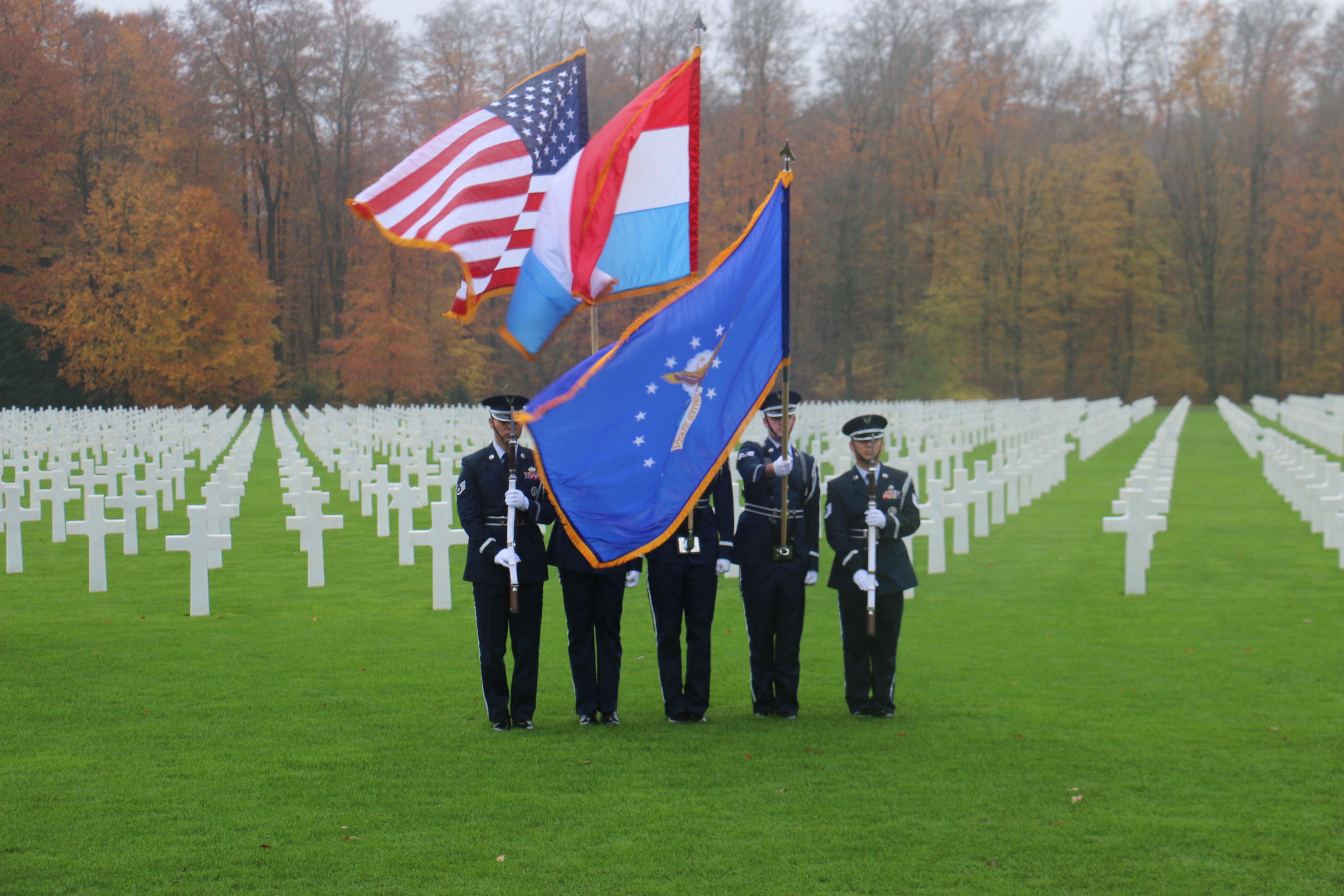 Honor Guard participants stand with firearms or flags in the plot area. 