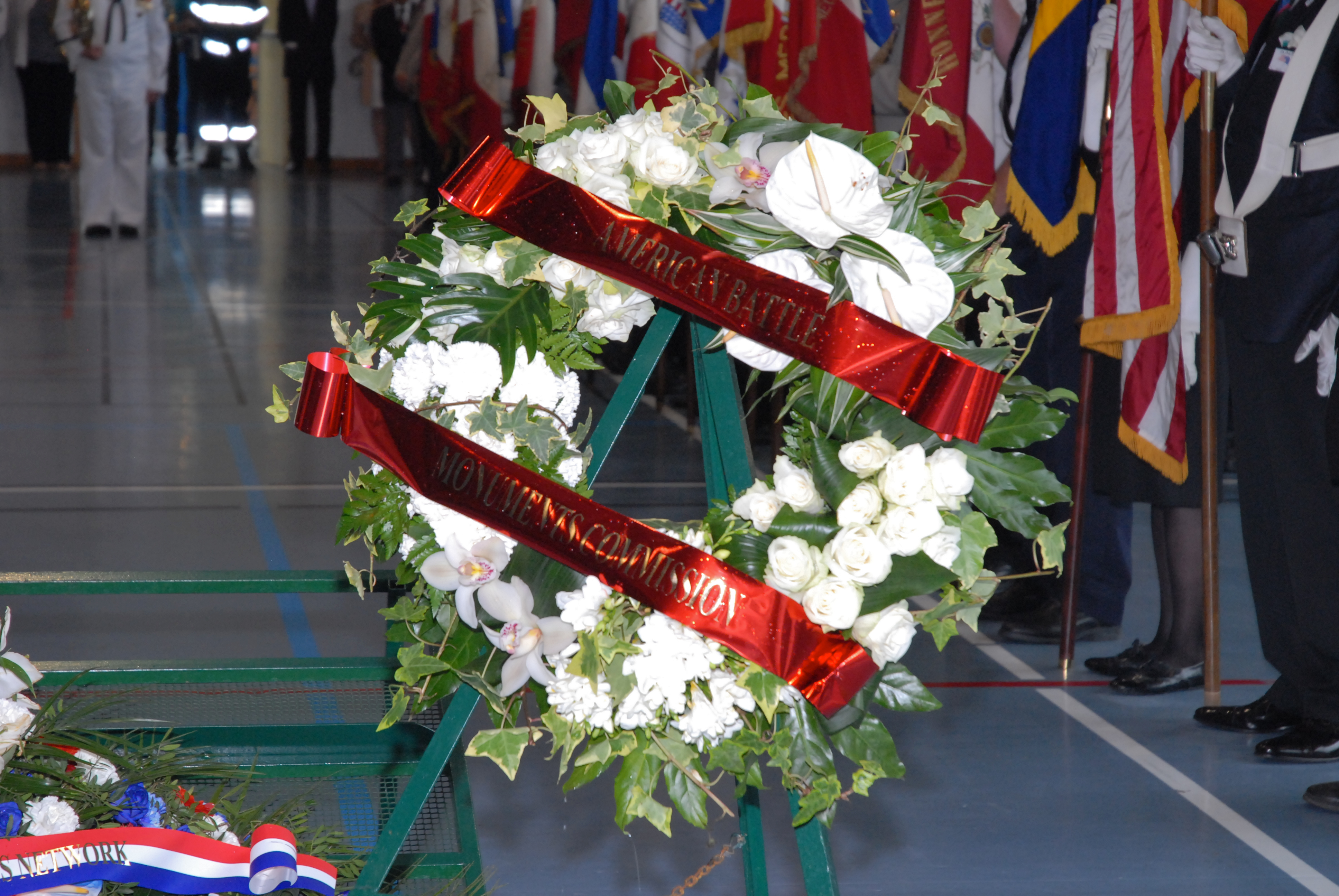 A floral wreath from the American Battle Monuments Commission rests on a stand. 