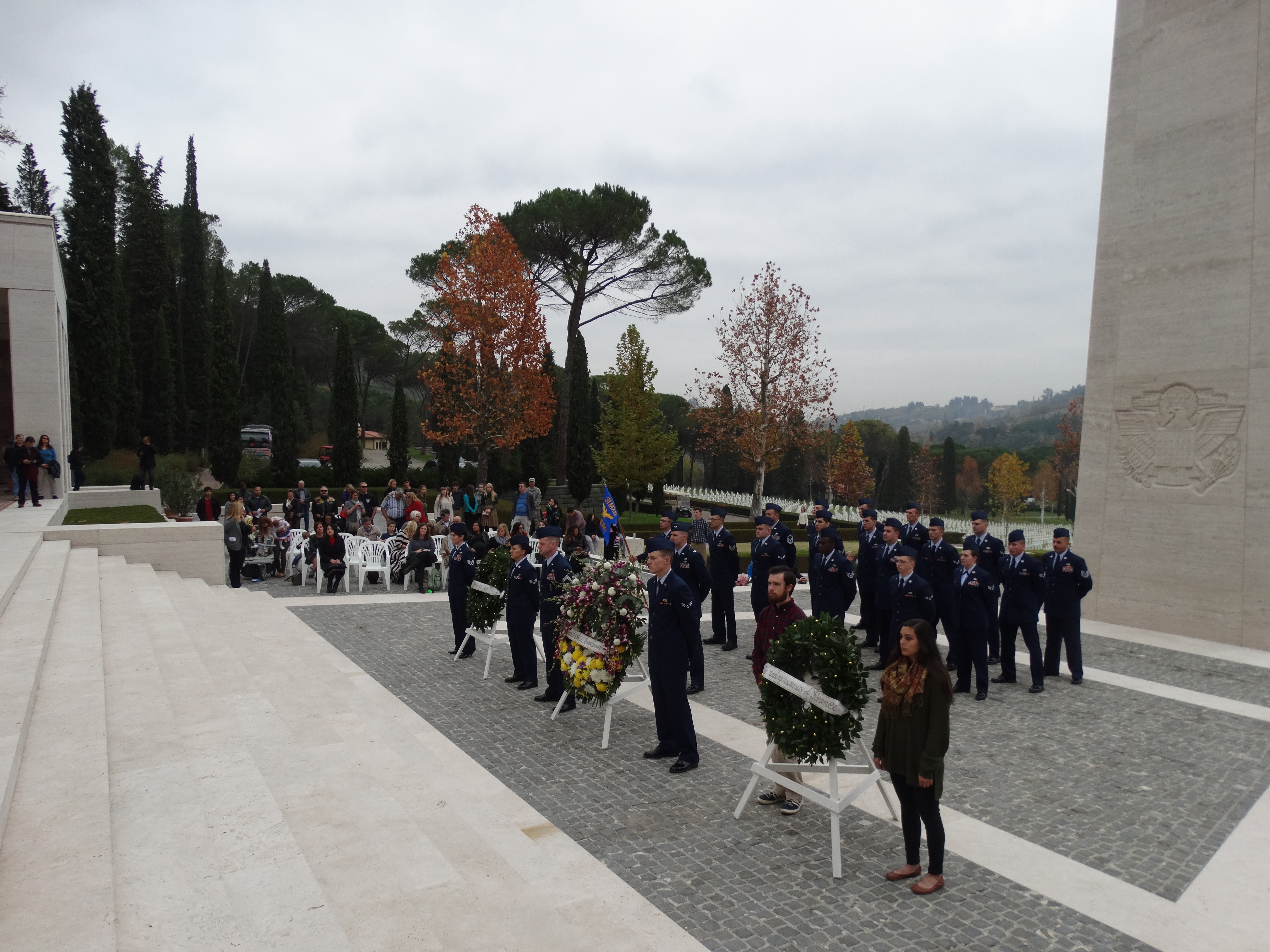 Members of the military along with two students stand next to floral wreaths. 
