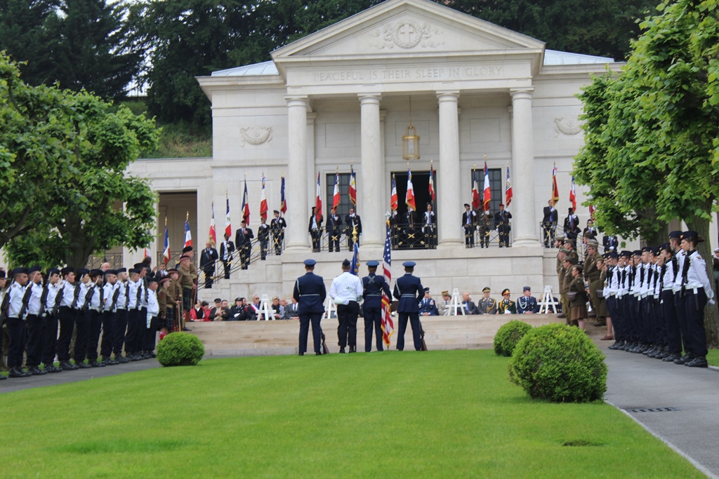 Flag bearers and men and women in uniform stand in front of the memorial building during the ceremony. 