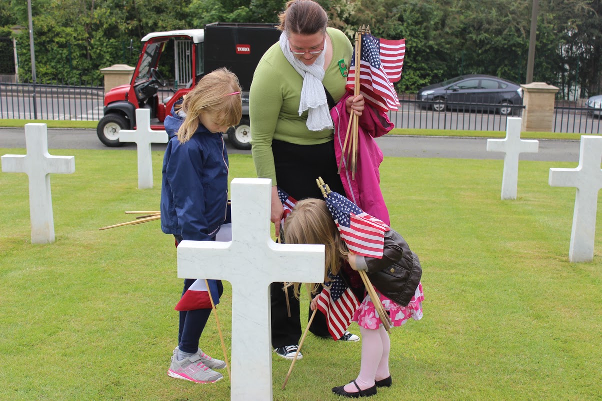 A woman and two children help to place the American and French flags in front of a headstone. 