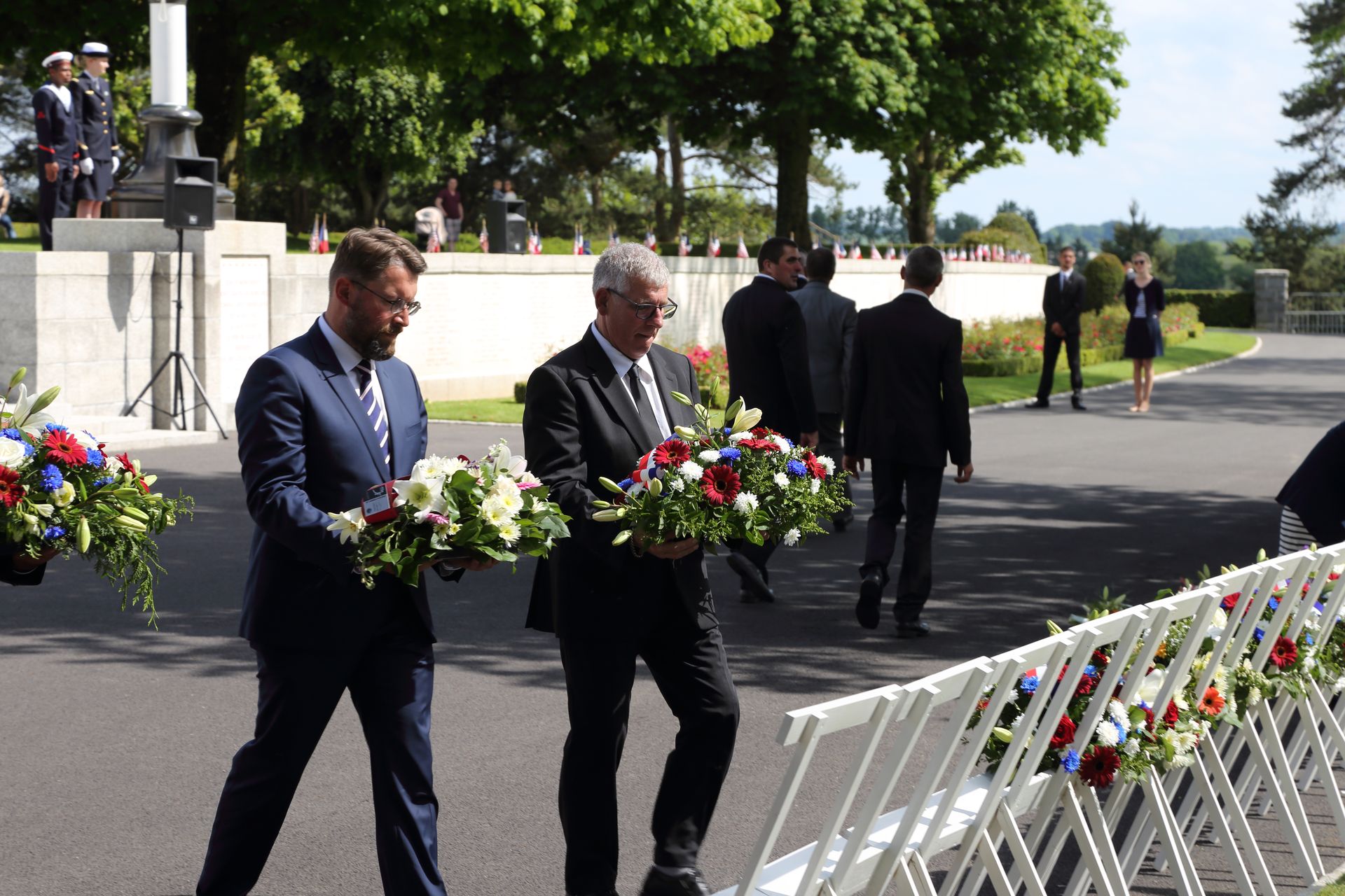 Two men carry floral wreaths to be laid. 