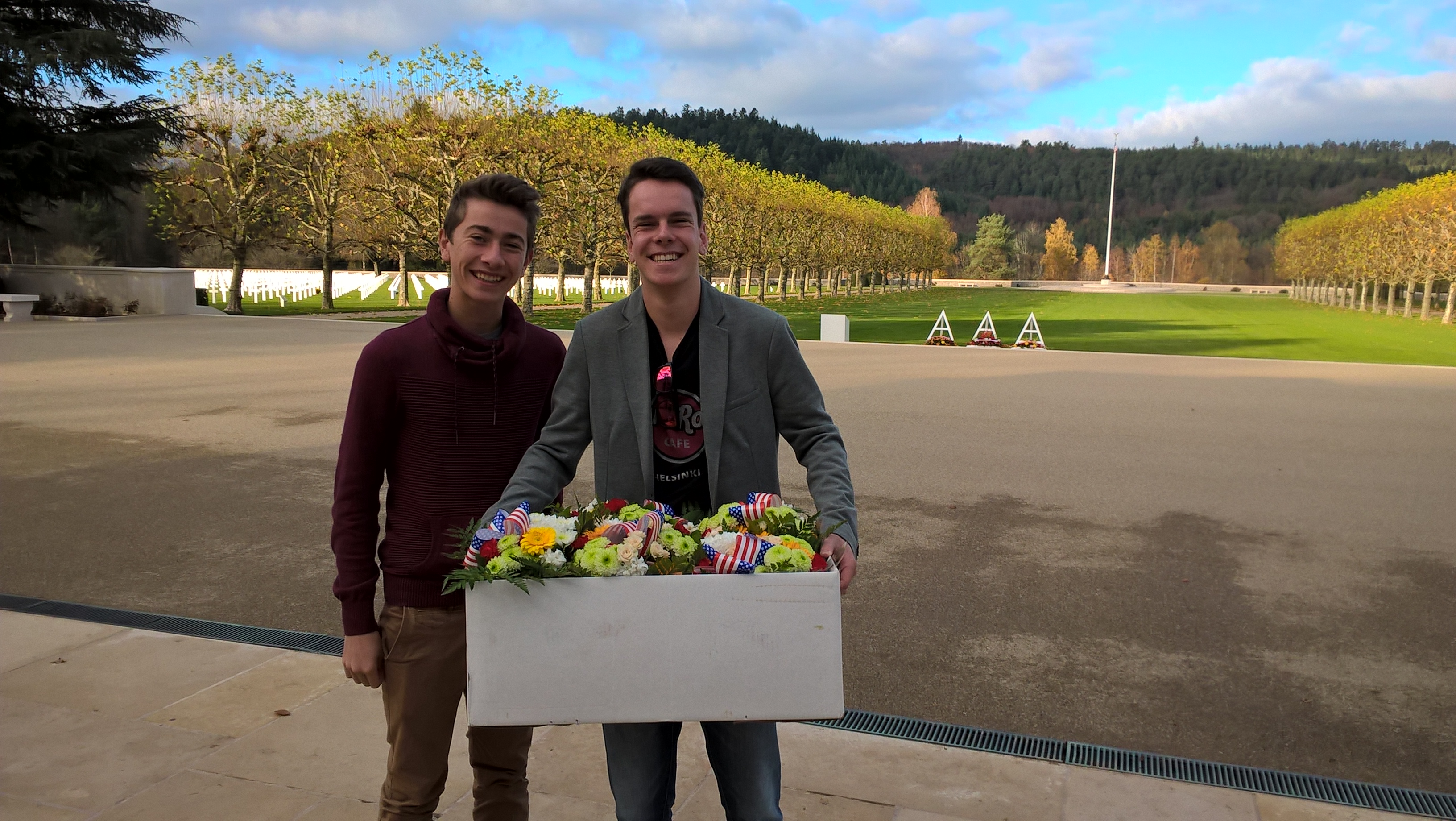 Two men stand with a box filled with flowers, ready to place them at gravesites.