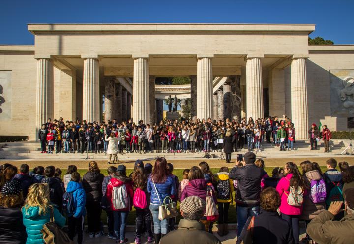 A large group of students stand on the steps of the memorial building to sing.