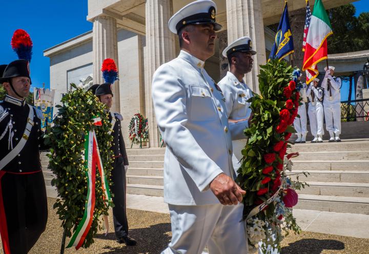 Men in uniform carry floral wreaths.