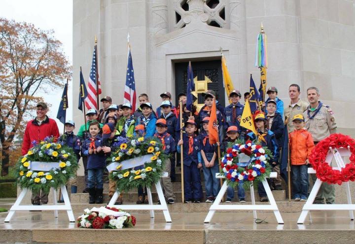 Boy Scouts stand in front of the chapel and behind the floral wreaths.
