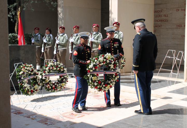 Two Marines present a floral wreath to a man in uniform. 