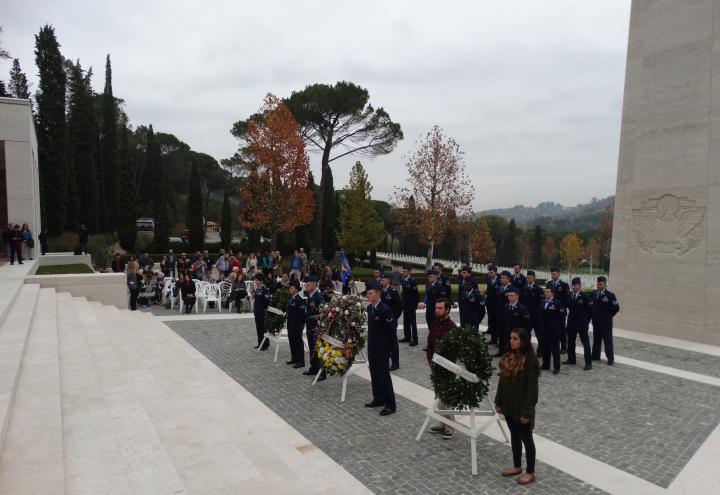 Members of the military along with two students stand next to floral wreaths. 