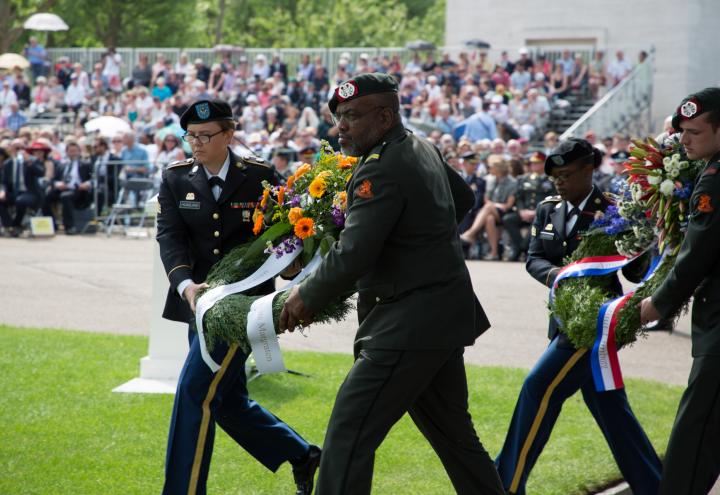 Men and women in uniform carry floral wreaths. 