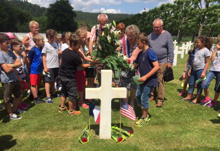 Students and adults place a larger flower arrangement at the headstone. 