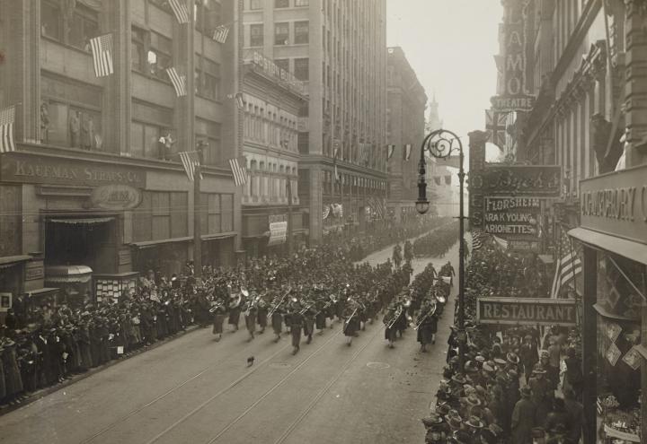 Historic photos shows men in uniform parading down city street.