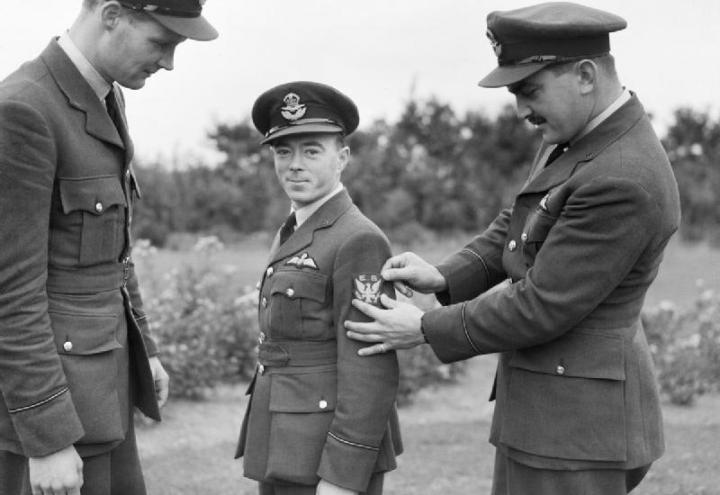 Historic photo of men in uniform with one receiving a patch on his arm. 