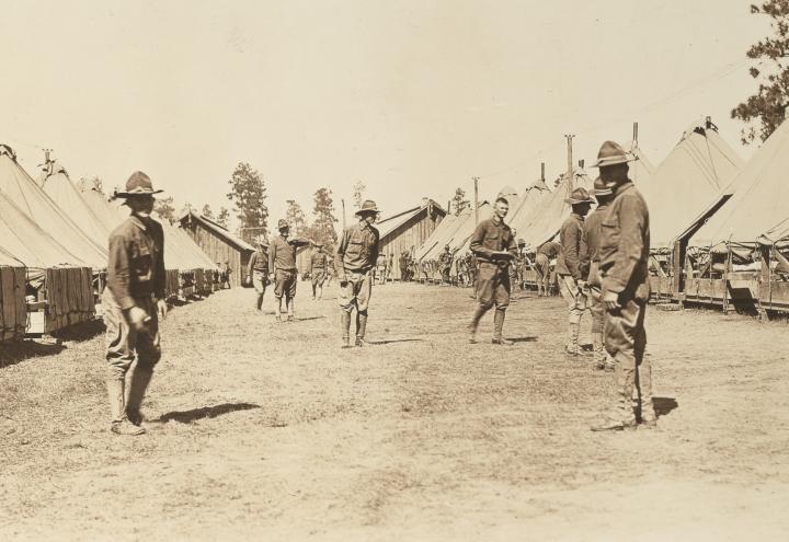 Historic photo shows soldiers in uniform standing near large tents. 