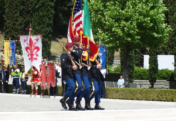 Men in uniform march out with flags and rifles.