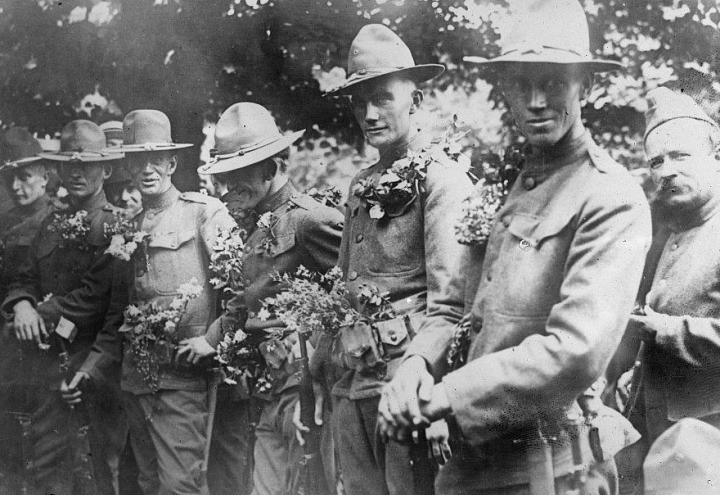 Historic photo shows soldiers in uniform with flowers. 
