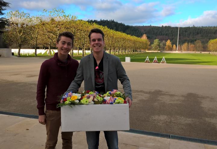 Two men stand with a box filled with flowers, ready to place them at gravesites.