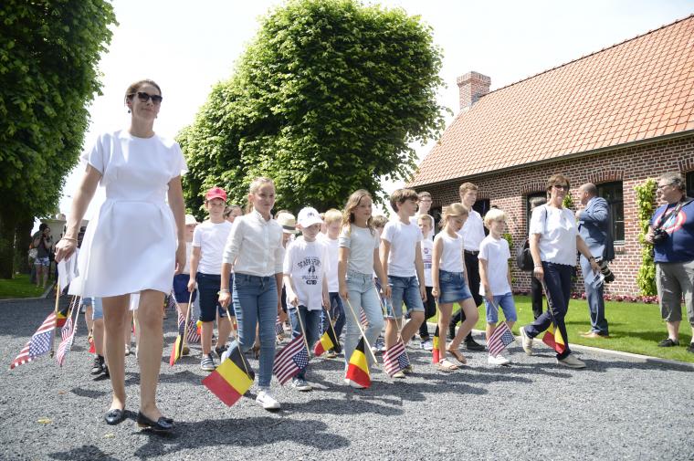 Children wearing white shirts march into the cemetery carrying flags.