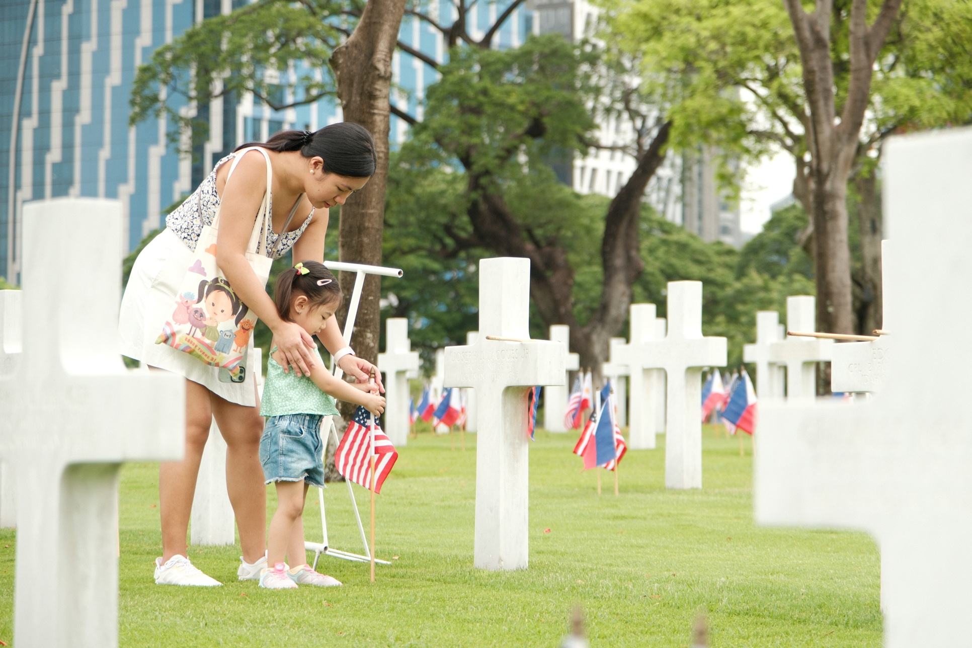 A mother and daughter place small American flags in front of headstones of World War II American fallen buried at Manila American Cemetery ahead of Memorial Day, 2024.