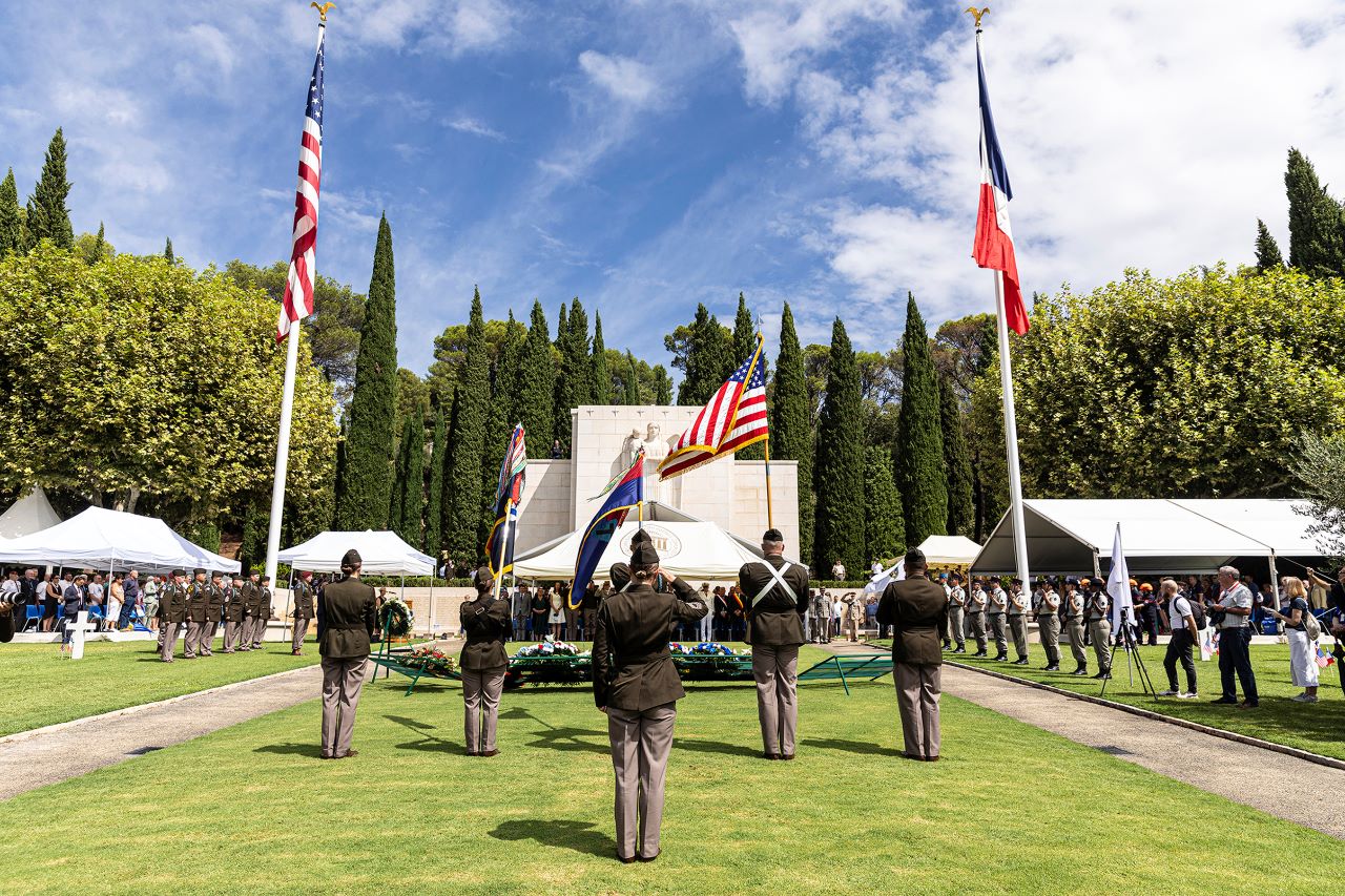 Soldiers facing the monument and ceremony guests salute during the playing of taps