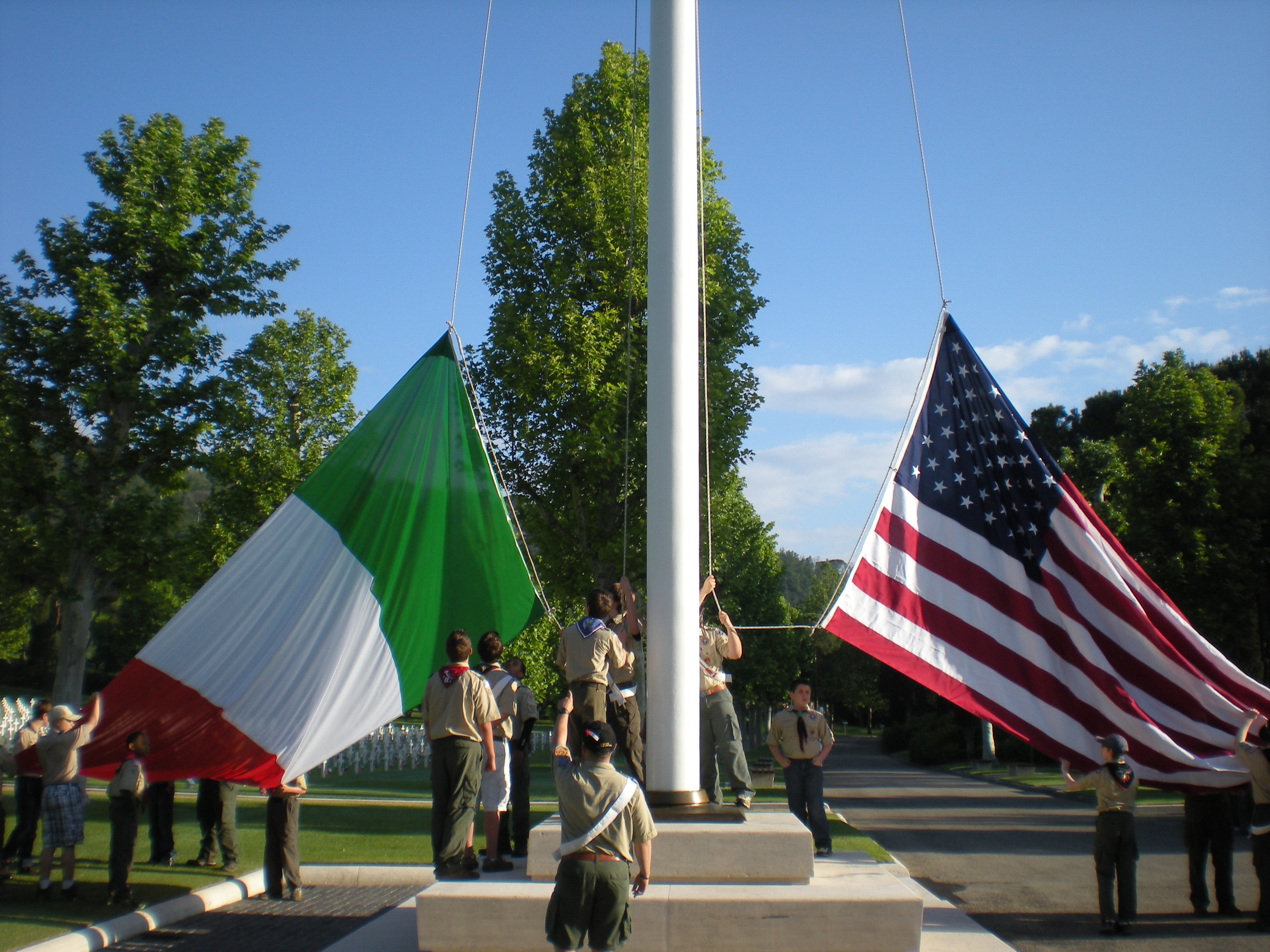 Boy Scouts raise large Italian and American flags on a flag pole.