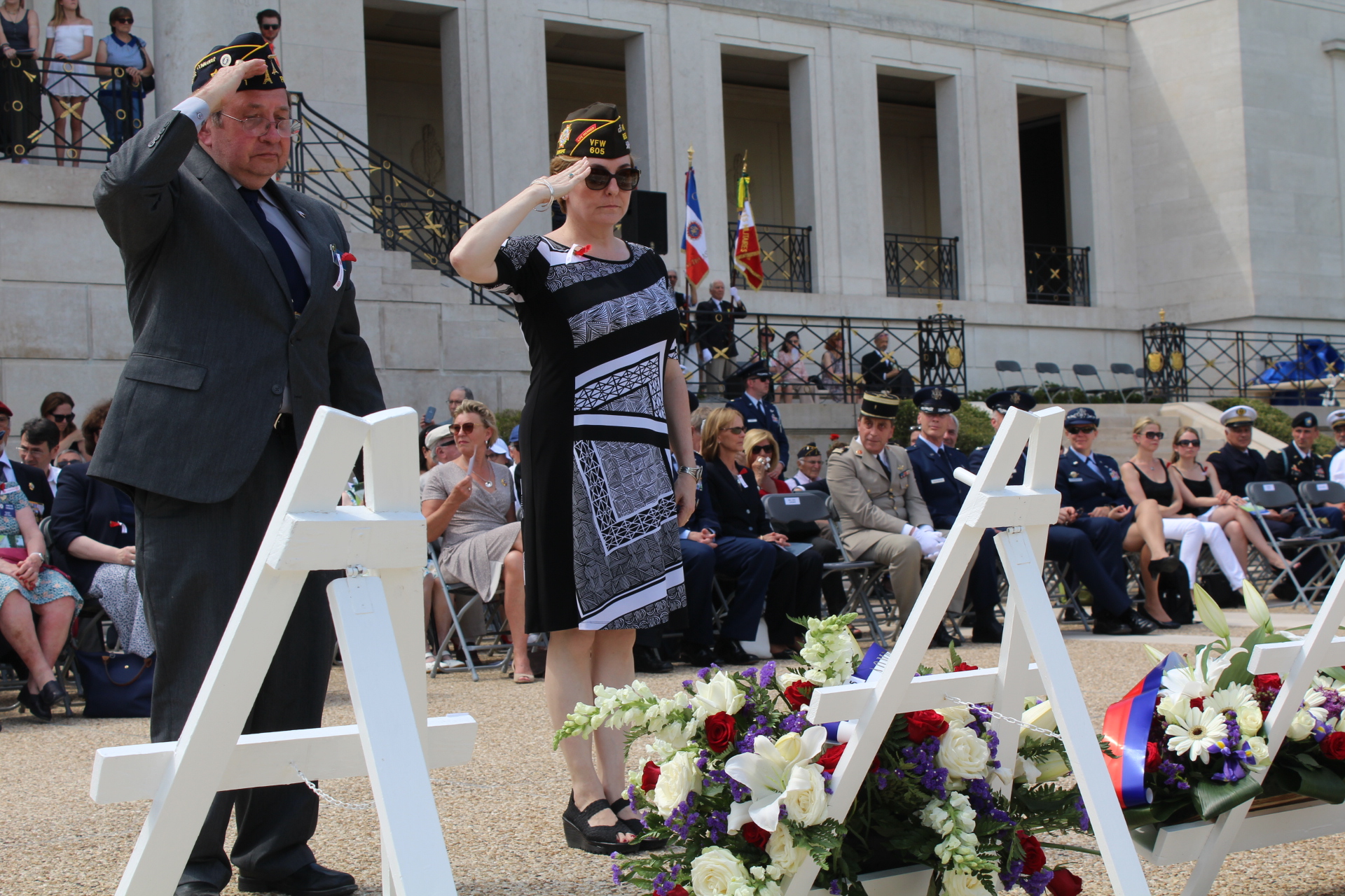 A man and woman salute after laying a wreath.