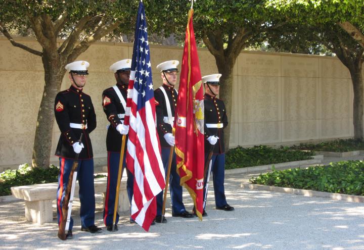 Marines stand with flags and weapons in front of the Wall of the Missing.