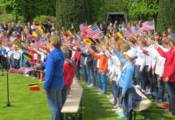 Rows of school children wave American and Belgian flags. 