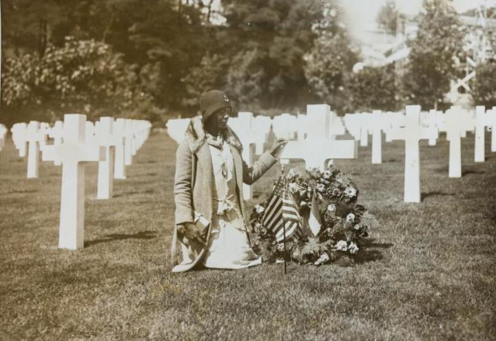 A woman kneels next to a headstone at Suresnes American Cemetery. 