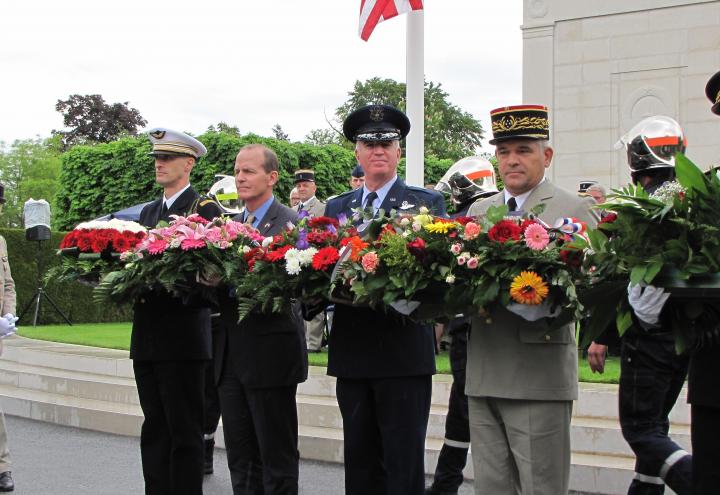 Men hold floral wreaths in preparation for wreath laying. 