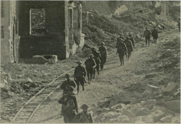 Historic image showing troops walking amongst the bombed out village of Varennes