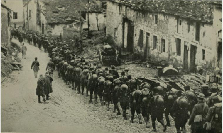 Historic image shows men in uniform marching through a ruined town. 