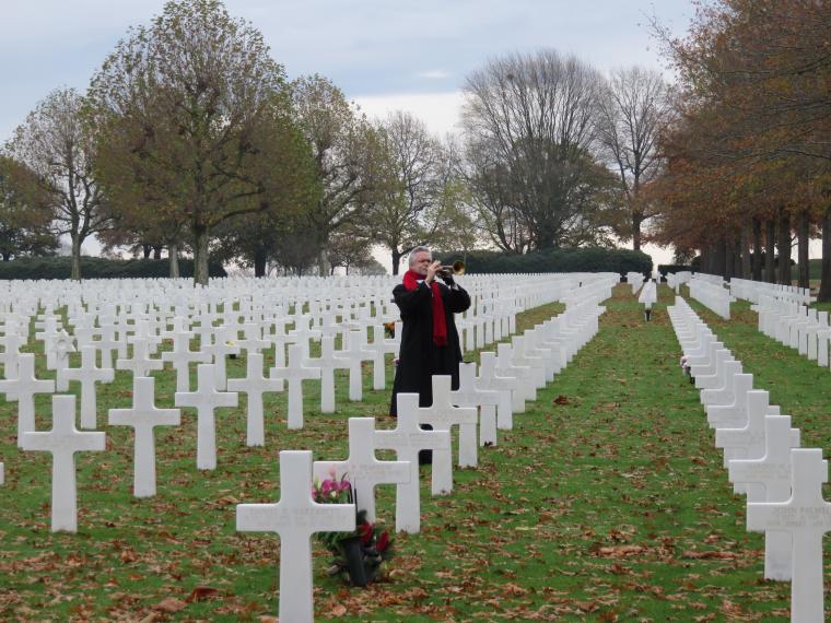 A bugler stands amongst the headstones, playing the bugle. 