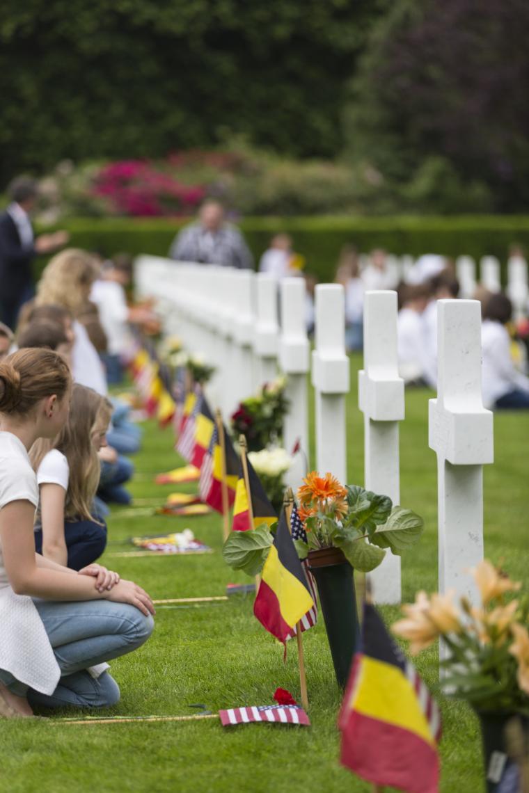 Students kneel next to the headstones with their flags.