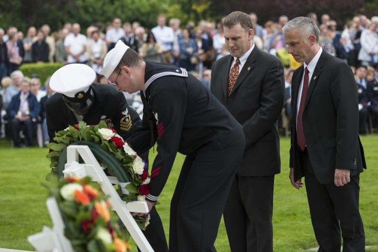 Men in uniform and suits lay a floral wreath. 