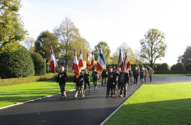Men carrying flags walk along the paved path in the cemetery.