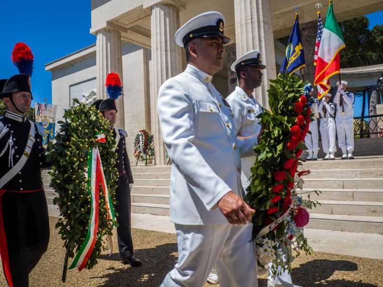 Men in uniform carry floral wreaths.