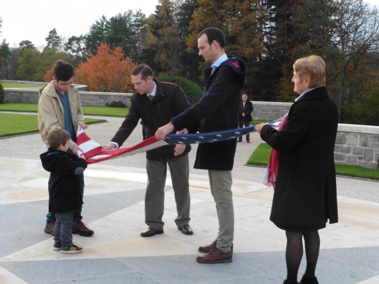 A young boy helps a four adults fold the American flag. 