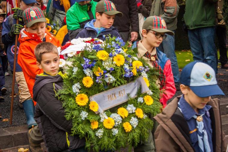 Boy Scouts carry a large floral wreath. 