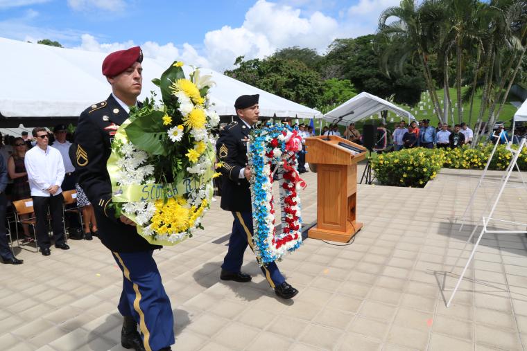 Members of the military in uniform carry large floral wreaths.