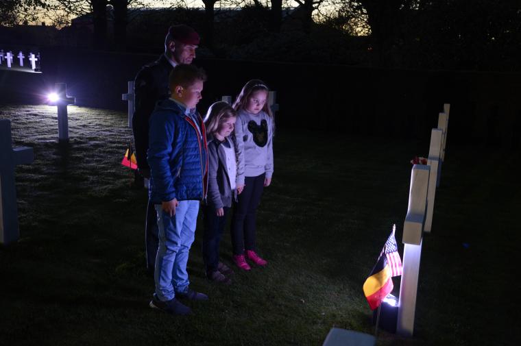 Kids and a man in uniform face a headstone as they reflect during the ceremony. 