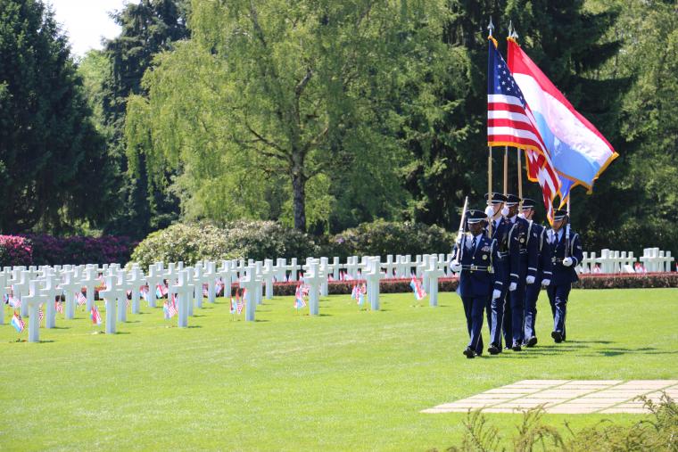 Men and women in uniform march through the cemetery.