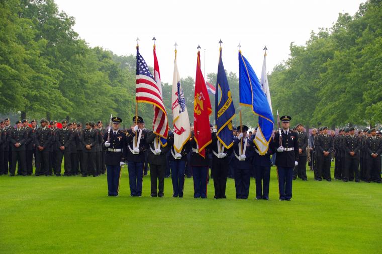 An American color guard stands in a straight line with flags and rifles. 