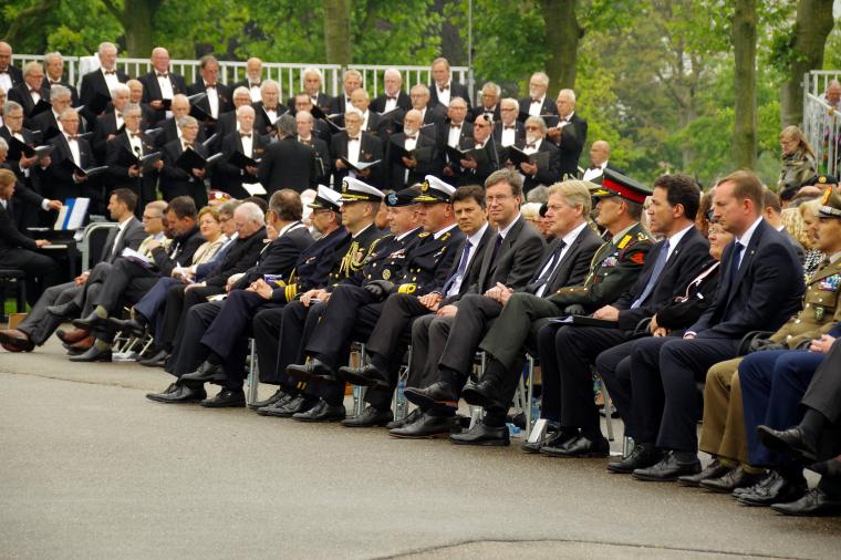 Men and women in uniforms and suits sit in the first row. 