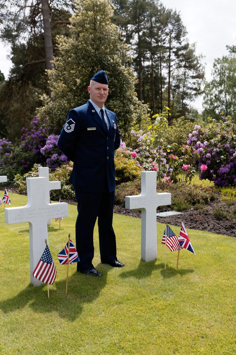 A man in uniform stands next to Latin cross headstones.