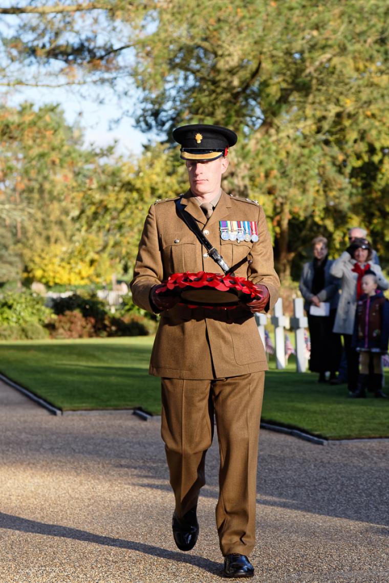 A man in uniform carries a wreath of poppies. 