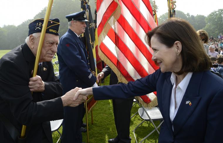 Ambassador Bauer shakes hands with a veteran holding the American flag. 