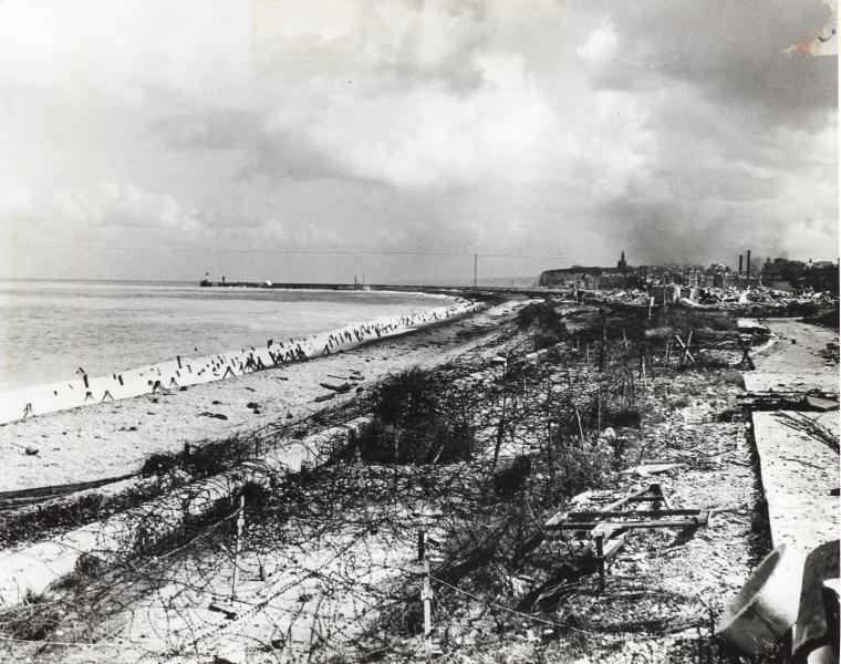 This historic image shows concrete barriers, wire fencing, and other obstacles on the beach. 